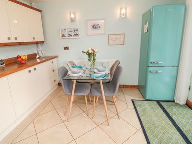 A kitchen with a glass dining table and chairs next to a turquoise fridge at Coast Cottage in Bamburgh