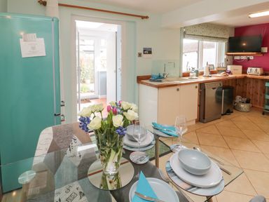 A kitchen with a glass dining table set with plates glasses and flowers a blue fridge and countertop appliances at Coast Cottage in Bamburgh