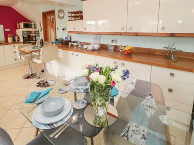 A kitchen with a glass dining table set with plates and a vase of flowers at Coast Cottage in Bamburgh