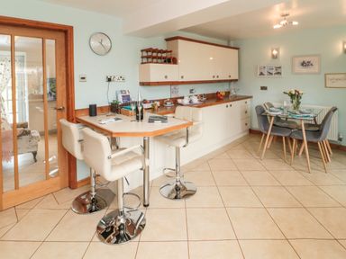 A kitchen with a breakfast bar with stools and a dining table with chairs at Coast Cottage in Bamburgh