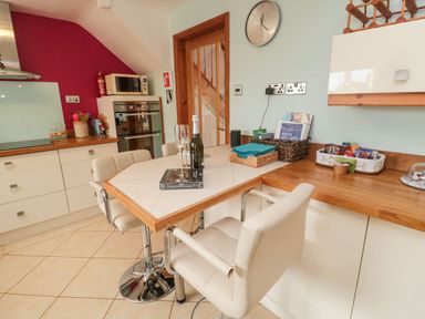 A kitchen with a dining counter and chairs a double oven and microwave a clock on the wall at Coast Cottage in Bamburgh