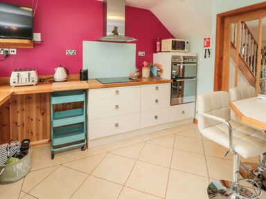 A kitchen with white cabinets a pink wall a wooden countertop a toaster kettle microwave oven and cream chairs at Coast Cottage in Bamburgh