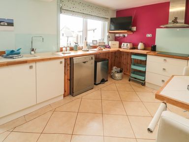 A kitchen with white cabinets wooden countertops dishwasher and window at Coast Cottage in Bamburgh