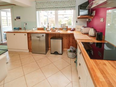 A kitchen with cream cabinets wooden countertops dishwasher trash bin and window at Coast Cottage in Bamburgh