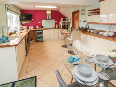 A kitchen with white cabinets wooden countertops a small dining table and a glass dining table set with dishes at Coast Cottage in Bamburgh