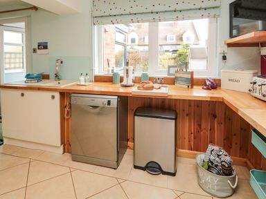 A kitchen with wooden countertops a dishwasher a trash bin a loaf of bread and a window at Coast Cottage in Bamburgh