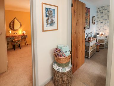 A hallway with a wicker basket of towels and two rooms with desks and chairs at Coast Cottage in Bamburgh