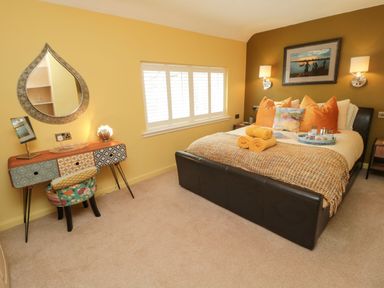 A bedroom with a bed with orange and multicolored pillows a patterned blanket and rolled towels a desk with a patterned chair and a decorative mirror at Coast Cottage in Bamburgh