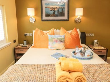 A bedroom with a bed with orange pillows and folded towels at Coast Cottage Bamburgh