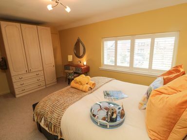 A bedroom with a bed with orange cushions and towels a wardrobe a decorated desk and a teardrop mirror at Coast Cottage in Bamburgh