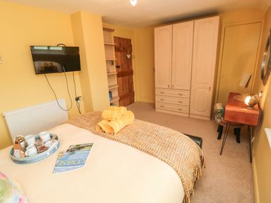 A bedroom with a wall-mounted TV a wooden wardrobe a desk and a bed with towels at Coast Cottage in Bamburgh