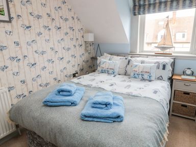 A bedroom with a bed covered with blue and white bedding and two sets of blue towels at Coast Cottage Bamburgh