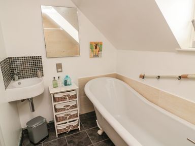 A bathroom with a bathtub a small sink a mirror and a storage unit with baskets at Coast Cottage Bamburgh