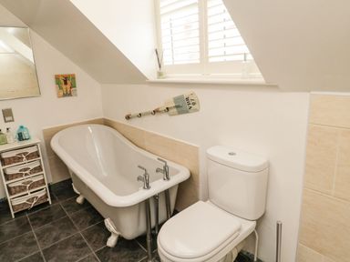 A bathroom with a bathtub and a toilet under a window with shutters at Coast Cottage in Bamburgh