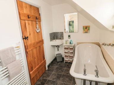 A bathroom with a white bathtub a wooden door towels on a rack and a small sink at Coast Cottage in Bamburgh