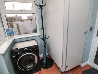 A utility room with a washing machine a coat rack with an umbrella and white cabinets at Coast Cottage in Bamburgh