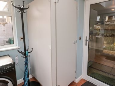 A utility room with a coat stand holding an umbrella a washing machine a window and a glass door at Coast Cottage in Bamburgh