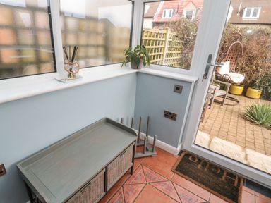 A small indoor space with a bench and a shoe rack next to a glass door leading to a patio with a hanging chair and plants at Coast Cottage in Bamburgh