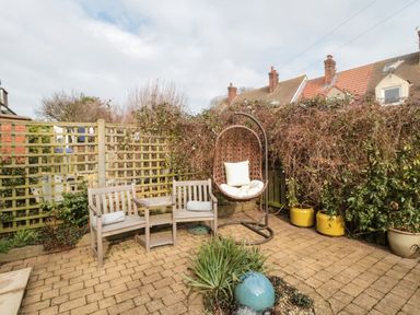 A garden patio with wooden bench seating a hanging chair potted plants and trellis fencing at Coast Cottage in Bamburgh