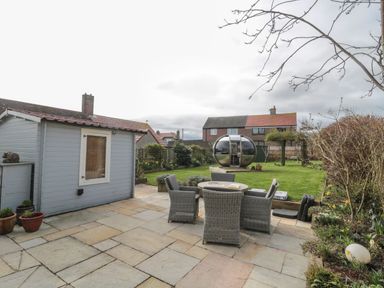 A backyard with a stone patio furniture and a modern pod structure at Coast Cottage in Bamburgh