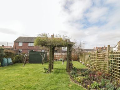 A garden with a wooden pergola a green shed and a flower bed at Coast Cottage Bamburgh