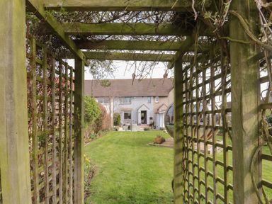 A wooden pergola overlooking a backyard with grass and a house in the background at Coast Cottage in Bamburgh