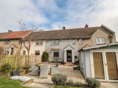 A patio with outdoor seating and a garden shed behind a terraced house at Coast Cottage Bamburgh