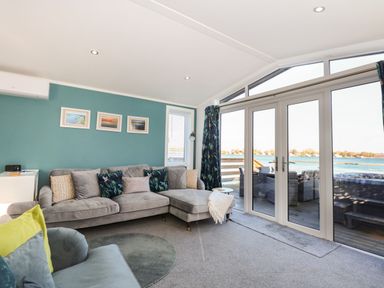 A living room with a grey sectional sofa and armchair facing glass doors with a view of water at Lake View Lodge in Tallington