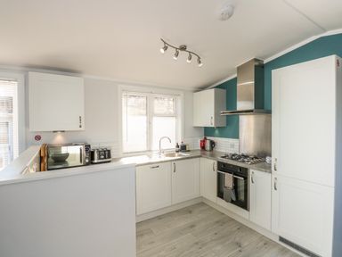 A kitchen with white cabinets a stove microwave toaster and sink at Lake View Lodge in Tallington