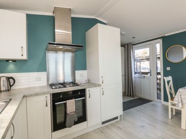 A kitchen with white cabinets a gas stove an oven a kettle and a table with chairs at Lake View Lodge in Tallington