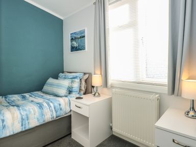 A bedroom with a single bed a bedside table with a lamp a radiator and a window at Lake View Lodge in Tallington