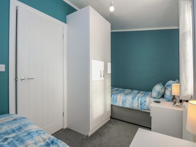 A bedroom with two single beds a white wardrobe a bedside table with a lamp and blue walls at Lake View Lodge in Tallington