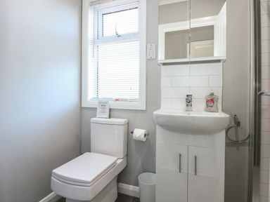 A bathroom with a toilet, sink with cabinet, mirror, window with blinds, and a shower at Lake View Lodge in Tallington