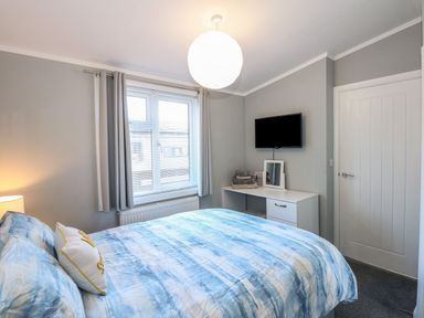 A bedroom with a bed a window a desk a mirror a television and folded towels at Lake View Lodge in Tallington