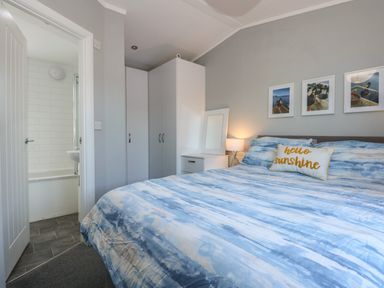A bedroom with a bed a wardrobe a bedside table with a lamp and a bathroom visible through an open door at Lake View Lodge in Tallington