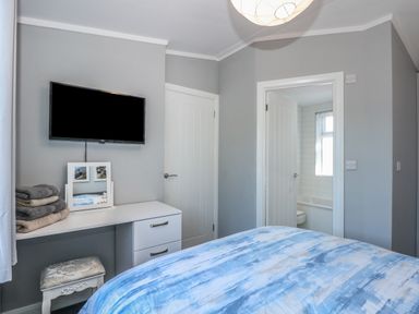 A bedroom with a bed, desk, mirror, towels, wall-mounted television, door to bathroom and white door at Lake View Lodge in Tallington
