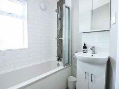 A bathroom with a bathtub shower unit sink cabinet mirror and window at Lake View Lodge in Tallington