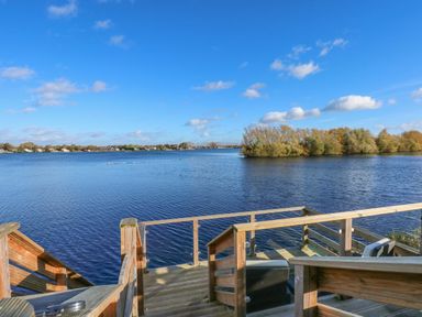 A wooden deck with stairs leading to a large lake with trees in the distance at Lake View Lodge in Tallington