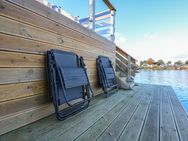 Two folded chairs leaning against wooden wall on a deck beside a lake with stairs leading up at Lake View Lodge in Tallington