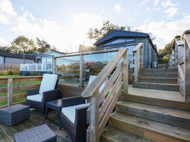 An outdoor wooden deck with wicker chairs and ottomans near a modern cabin at Lake View Lodge in Tallington