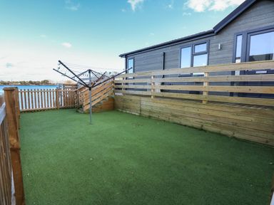 A fenced outdoor area with artificial grass clothesline and wooden railing by a building at Lake View Lodge in Tallington