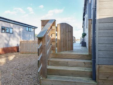 An outdoor wooden staircase with a gate leading to a wooden deck between two buildings at Lake View Lodge in Tallington
