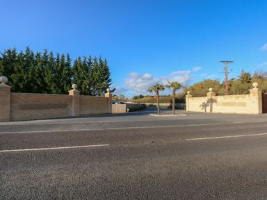 An entrance gate with brick pillars and palm trees along a road at Lake View Lodge in Tallington