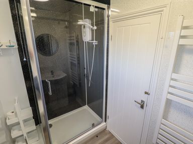 A bathroom with a glass shower enclosure a white door and a white towel rack at 114 Cherry Park in Chapel St Leonards