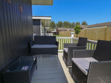 An outdoor patio with black wicker furniture including two chairs a loveseat and a glass top table with a fenced garden in the background at 114 Cherry Park in Chapel St Leonards
