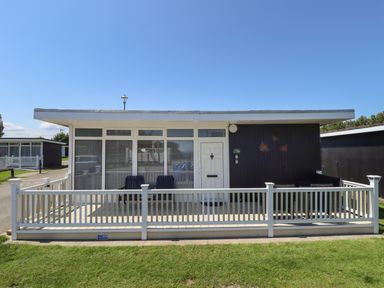 A single-story building with a white railing and two chairs on the porch at 114 Cherry Park in Chapel St Leonards