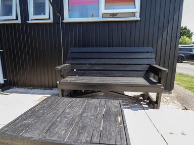 An outdoor wooden bench and table set on a patio outside a building with black vertical siding and small windows at 114 Cherry Park in Chapel St Leonards