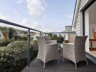 An outdoor balcony with four wicker chairs and a glass railing overlooking houses at Pebble Ridge View in Westward Ho