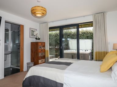 A bedroom with bed yellow pillows wooden chest of drawers and sliding glass door leading outside at Pebble Ridge View in Westward Ho