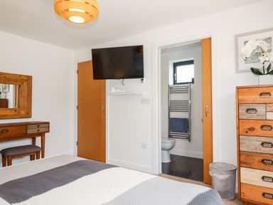 A bedroom with a bed a wooden dresser a wooden vanity with mirror a wall-mounted television and an en suite bathroom at Pebble Ridge View in Westward Ho